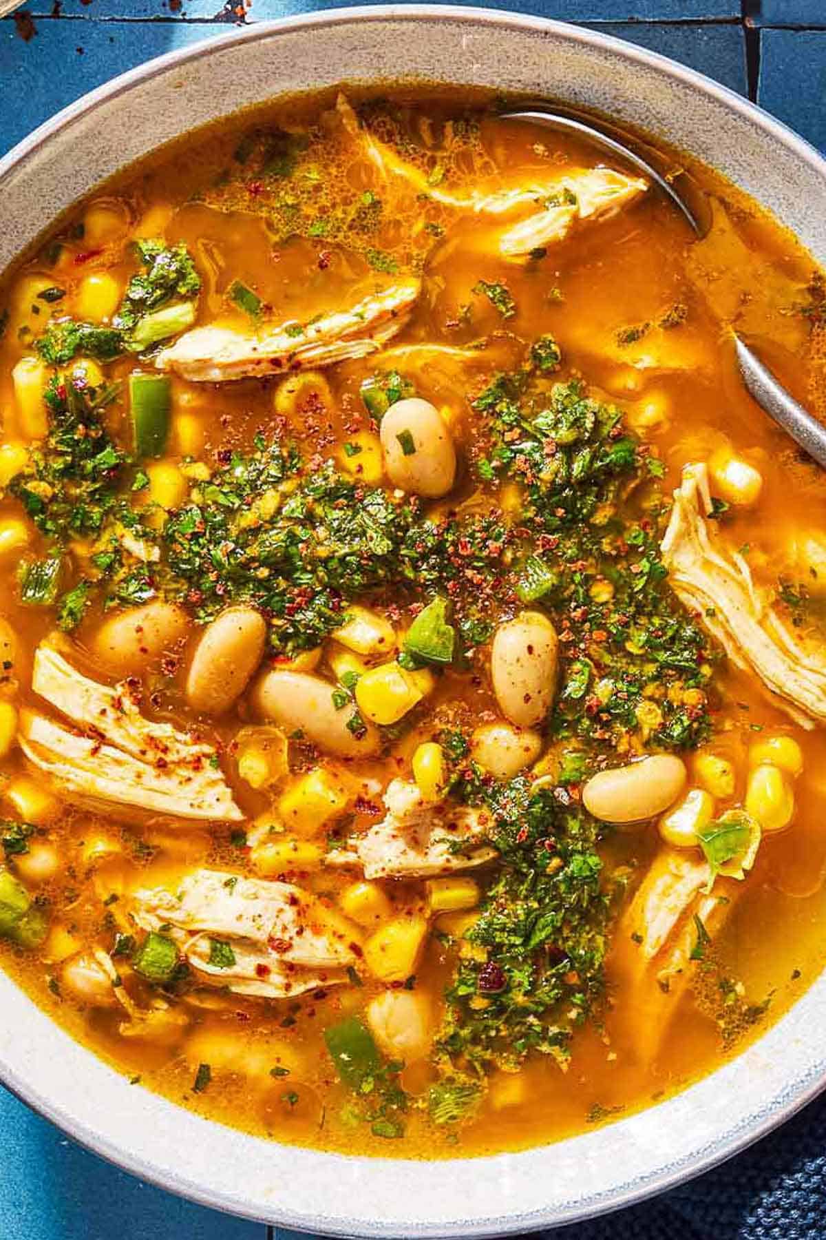 An overhead close up photo of white chicken chili topped with chermoula in a bowl with a spoon.