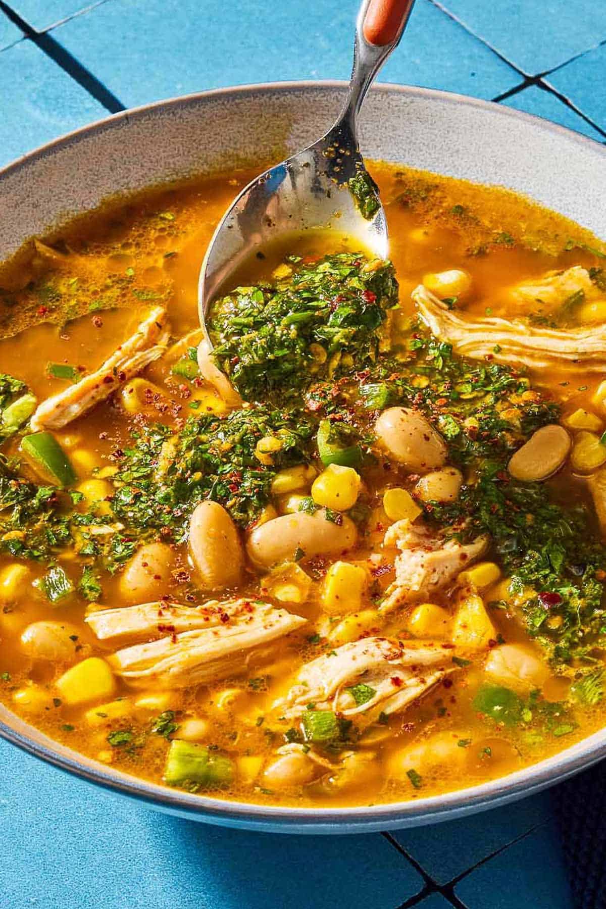 A close up of white chicken chili in a bowl being topped with chermoula with a spoon.