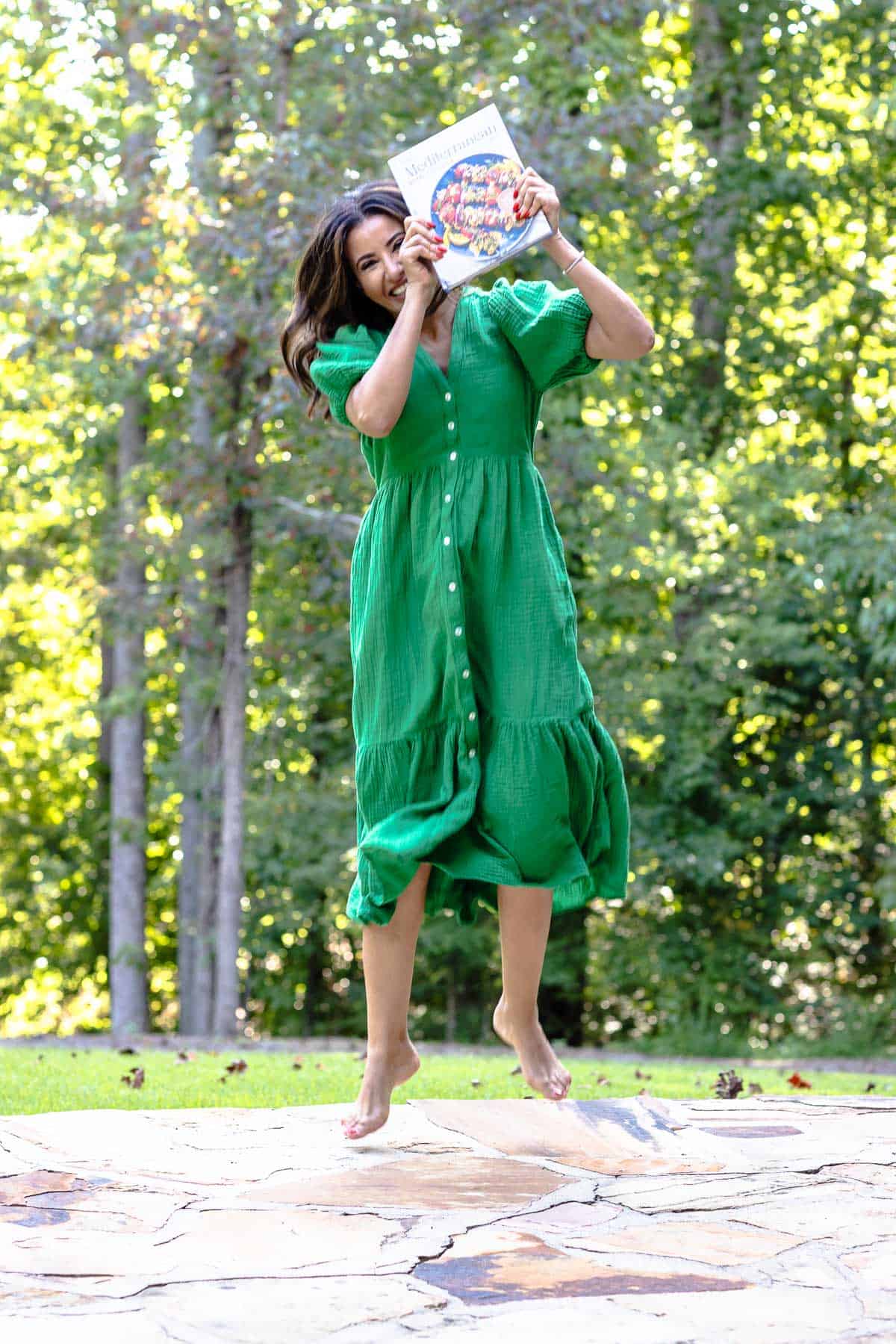 Suzy Karadsheh jumping while holding Simply Dinner Cookbook