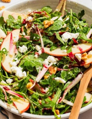 Apple walnut salad in a serving bowl with wooden serving utensils.