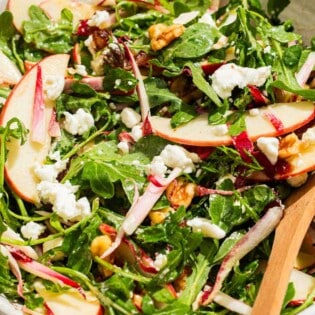 Apple walnut salad in a serving bowl with wooden serving utensils.