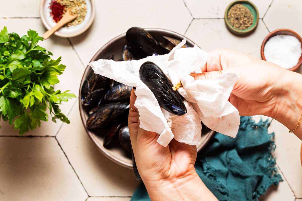 An overhead photo of the beard being removed from a mussel. In the background is the entire bowl of mussels, and the rest of the ingredients for the stew.