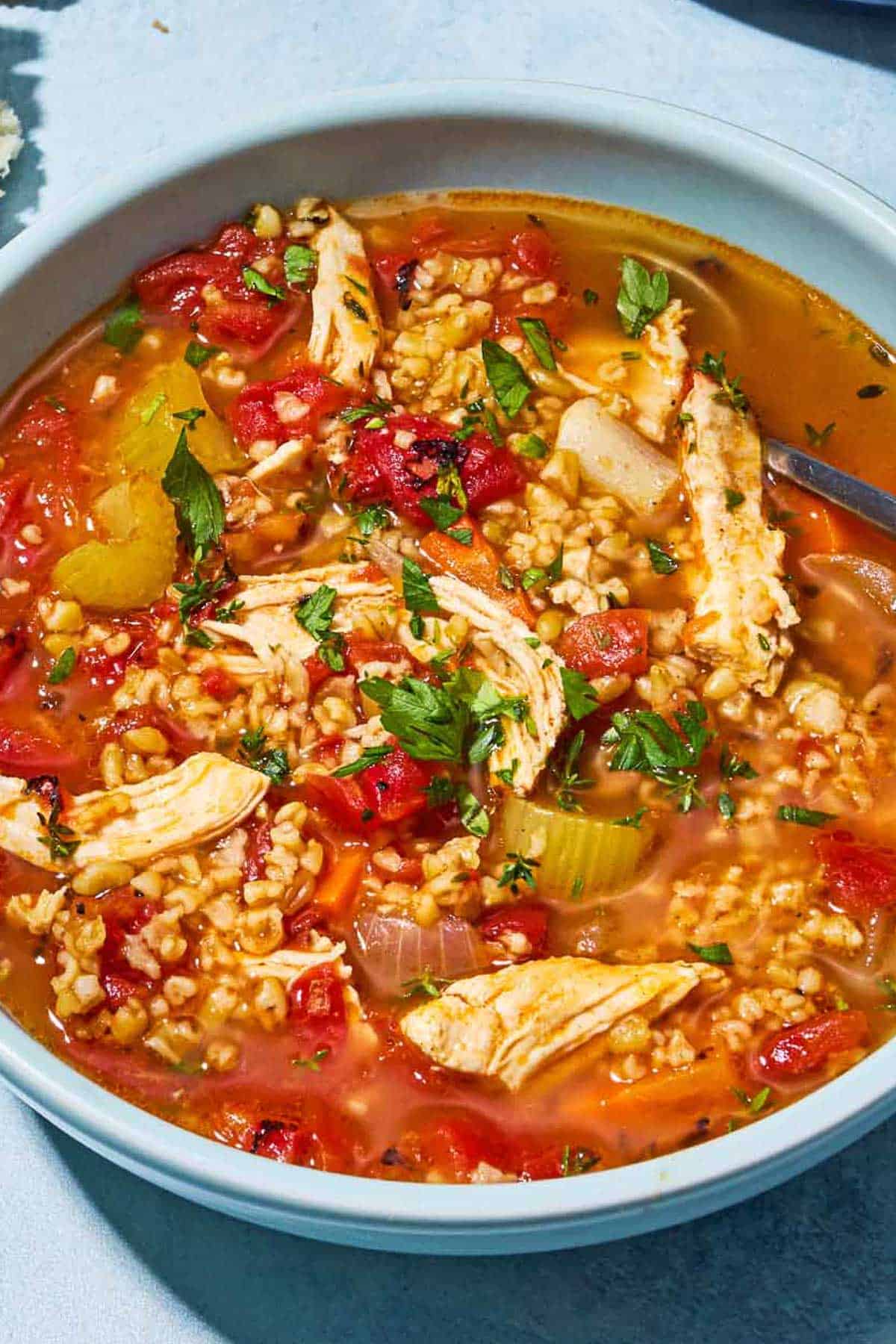 A close up of freekeh soup with chicken in a bowl with a spoon.