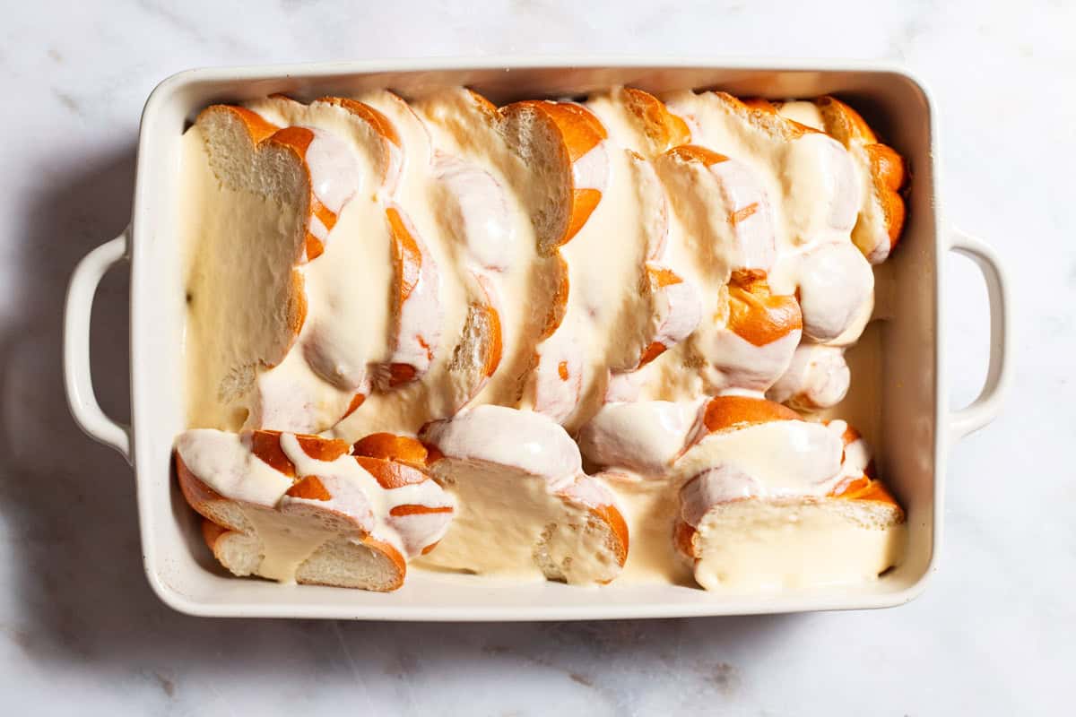 An overhead photo of slices of challah arranged in a baking dish topped with the custard.