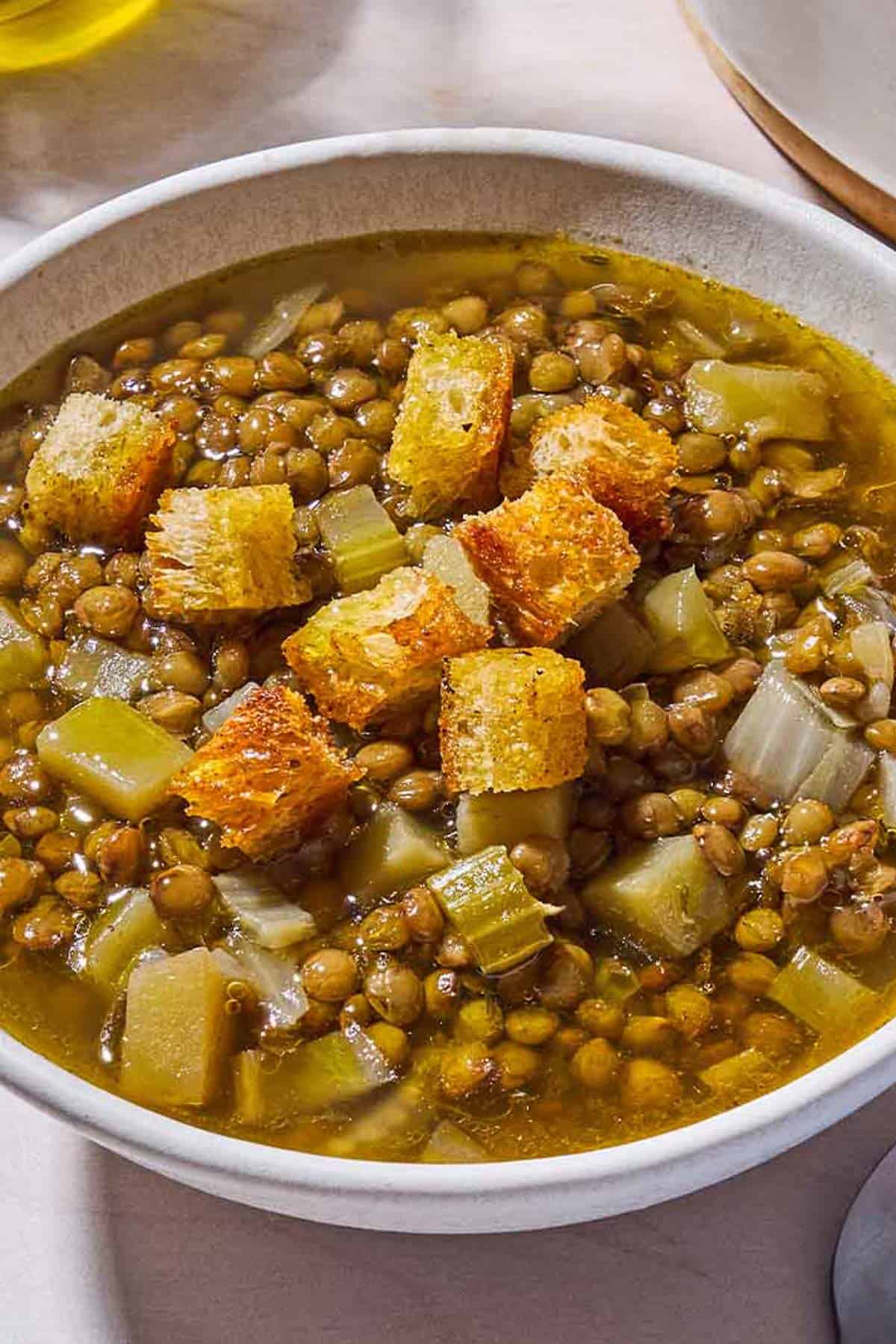 A close up of a bowl of lentil potato soup topped with croutons.