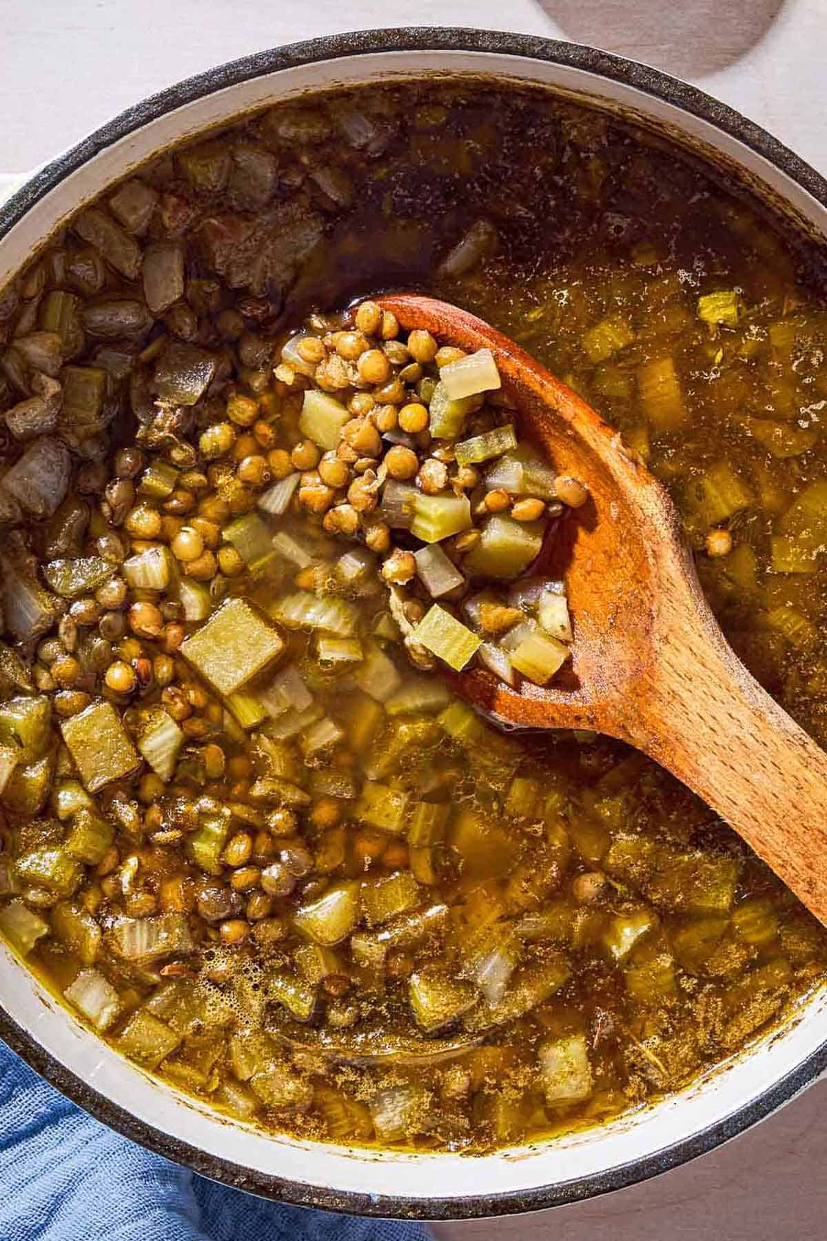 An overhead photo of a pot of lentil potato soup with a wooden spoon.