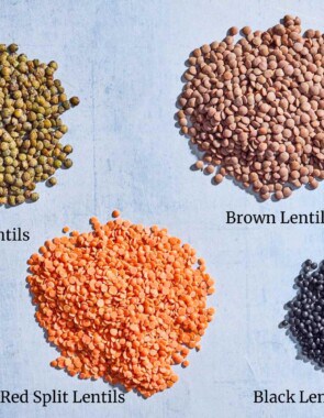 A close up of piles of brown lentils, black lentils, french green lentils and red split lentils.