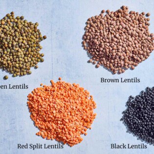 A close up of piles of brown lentils, black lentils, french green lentils and red split lentils.