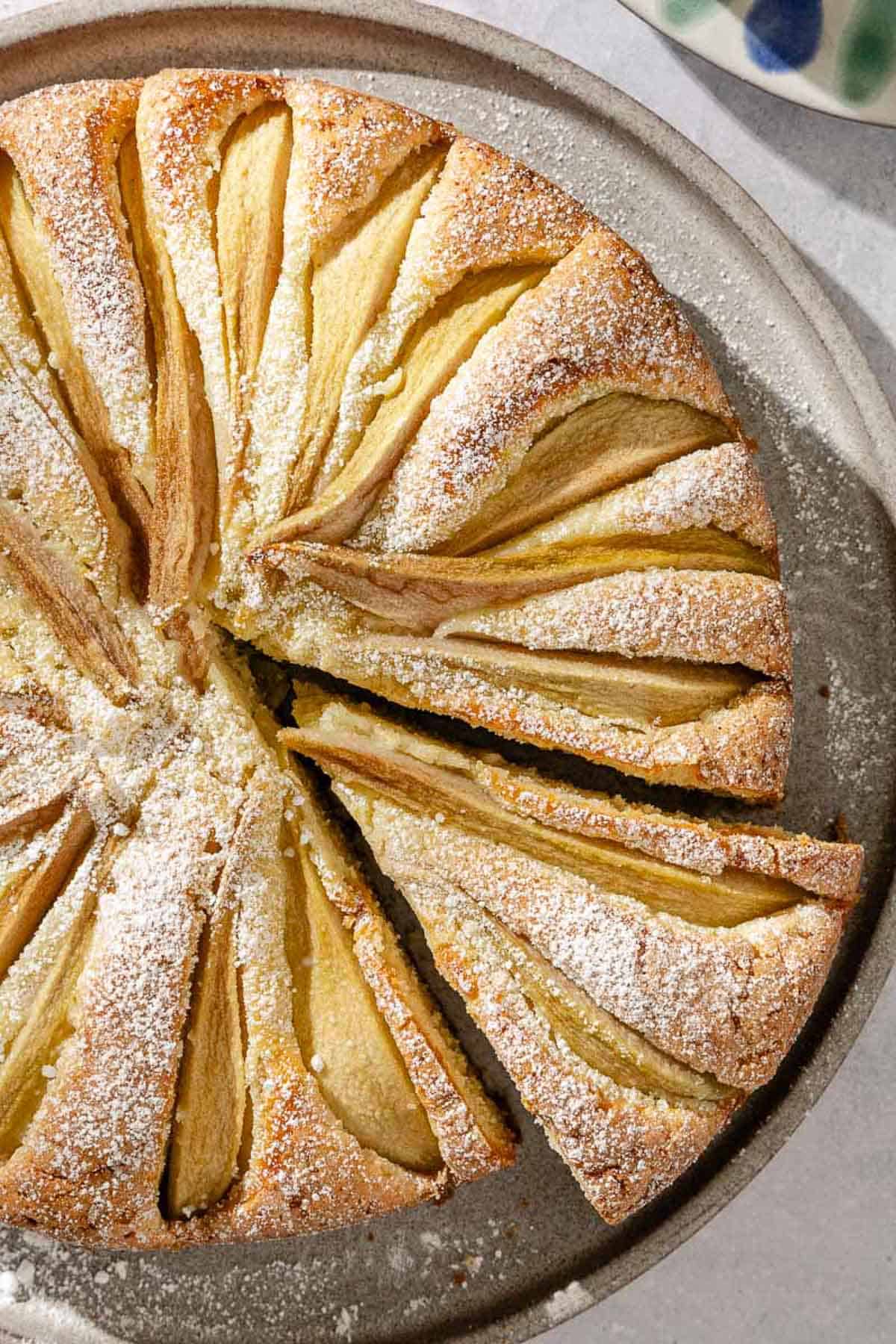 An Italian pear cake with one slice cut out of it on a serving platter.