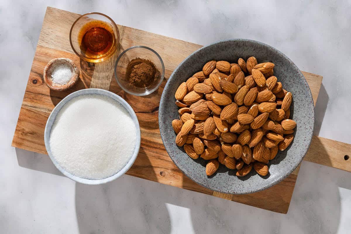 Ingredients for candied almonds including raw almonds, sugar, vanilla extract, kosher salt, and ground cinnamon.