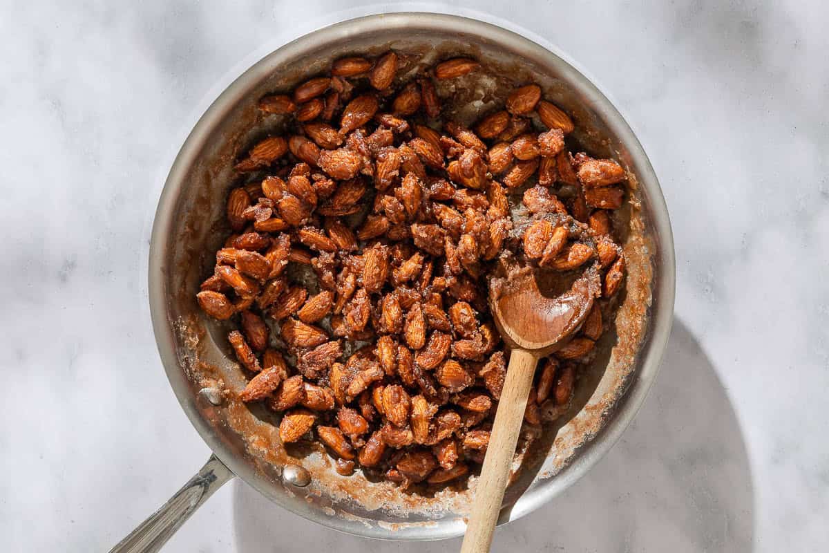 An overhead photo of the almonds caramelizing in a skillet with a wooden spoon.