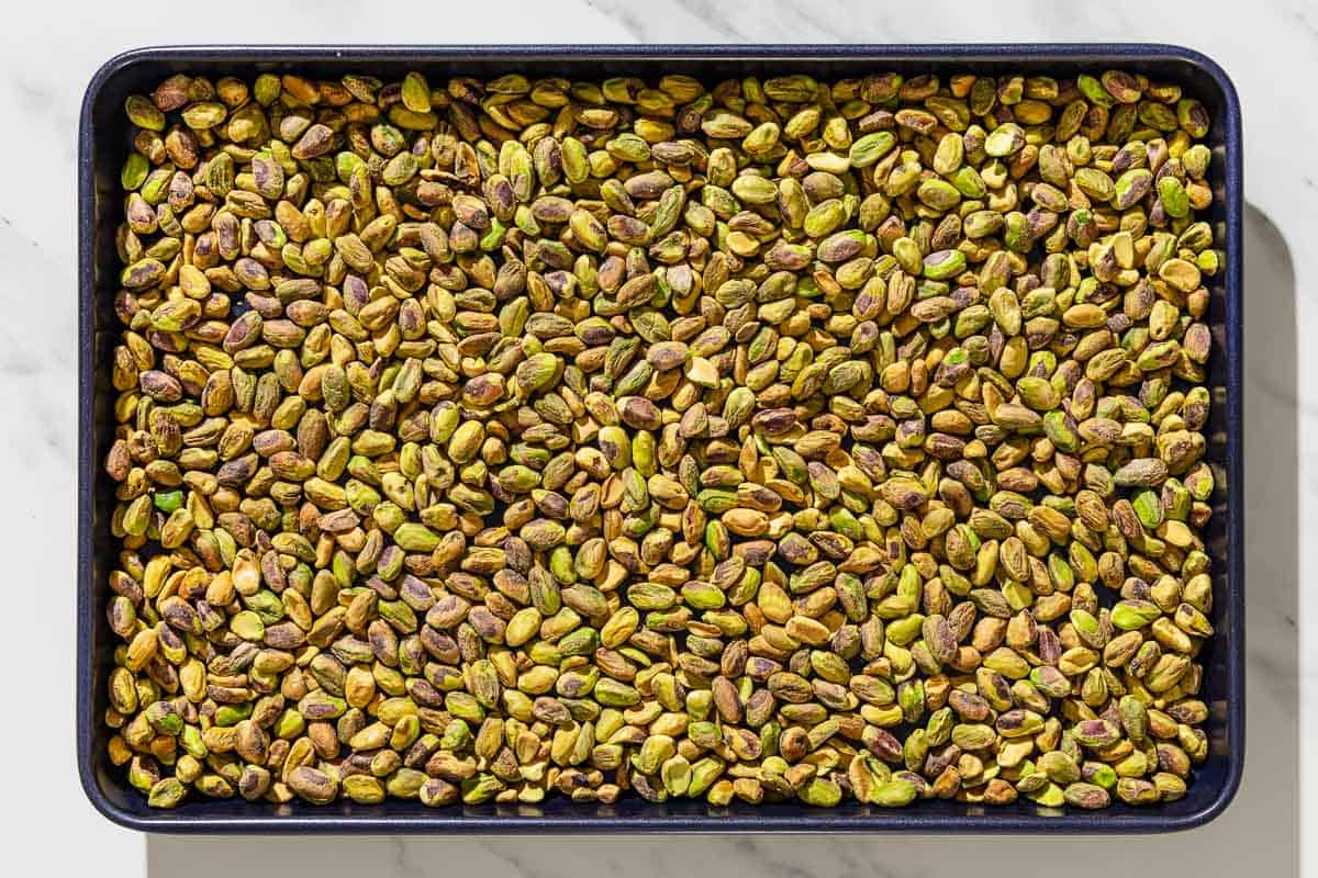 An overhead photo of raw pistachios spread evenly on a baking sheet.