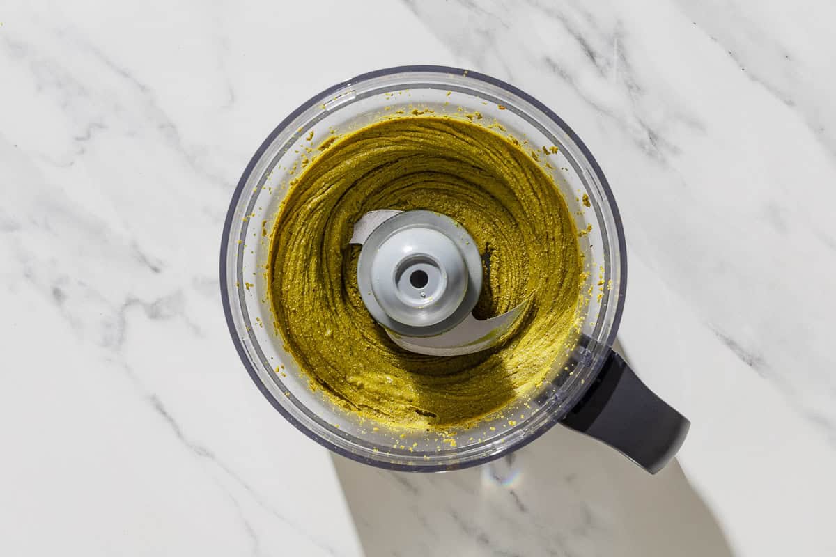 An overhead photo of pistachio butter in the bowl of a food processor fitted with a blade.