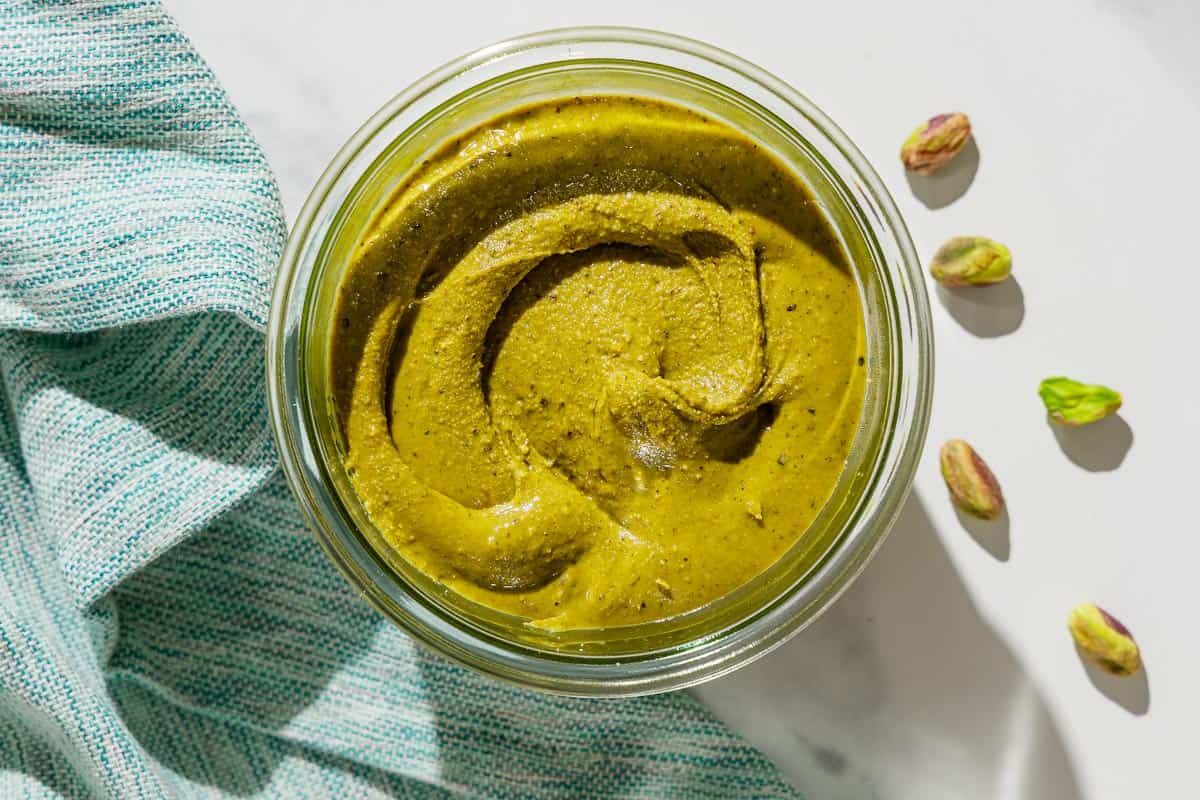 An overhead photo of pistachio butter in a bowl. Next to this is a cloth napkin and a few individual pistachios.