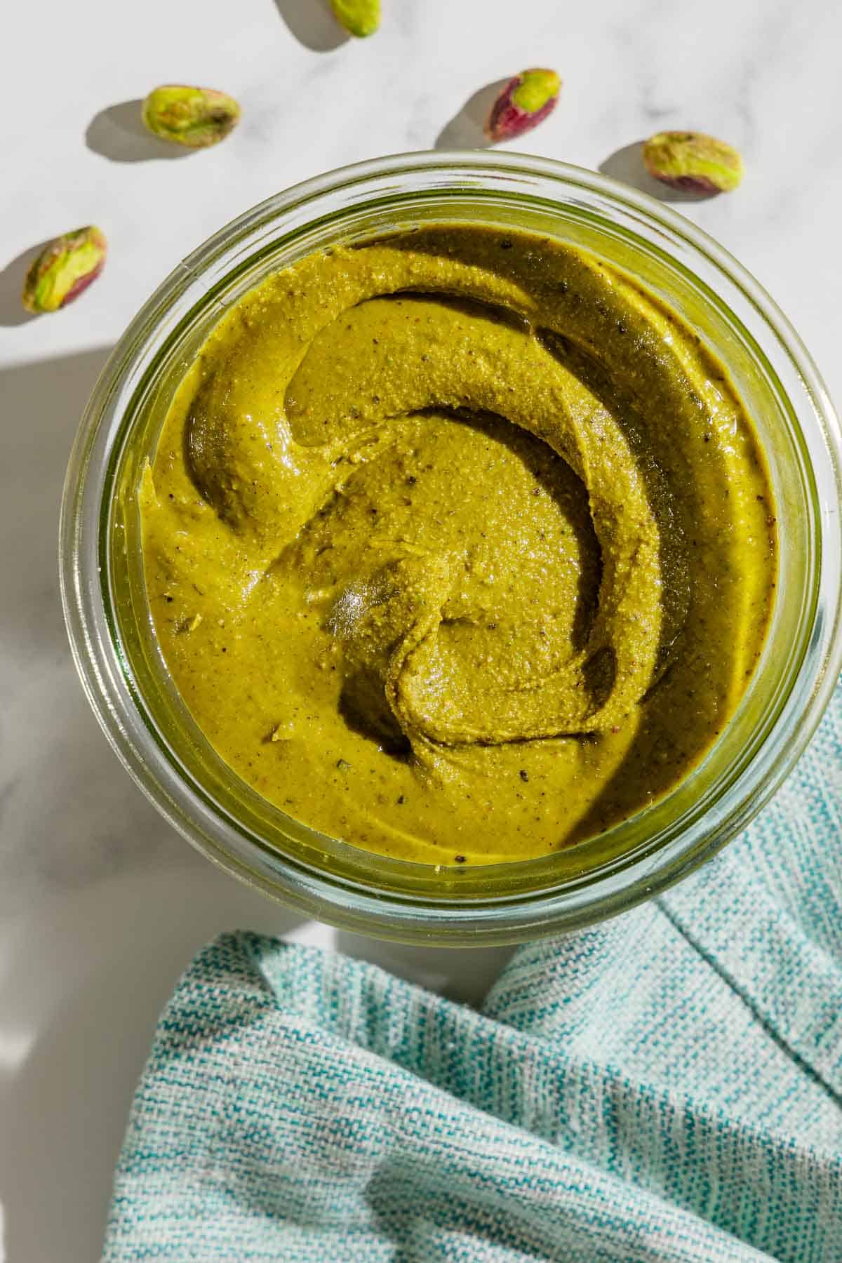 An overhead photo of pistachio butter in a bowl. Next to this is a cloth napkin and a few individual pistachios.