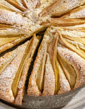 An Italian pear cake with one slice cut out of it on a serving platter.