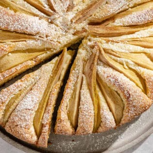 An Italian pear cake with one slice cut out of it on a serving platter.