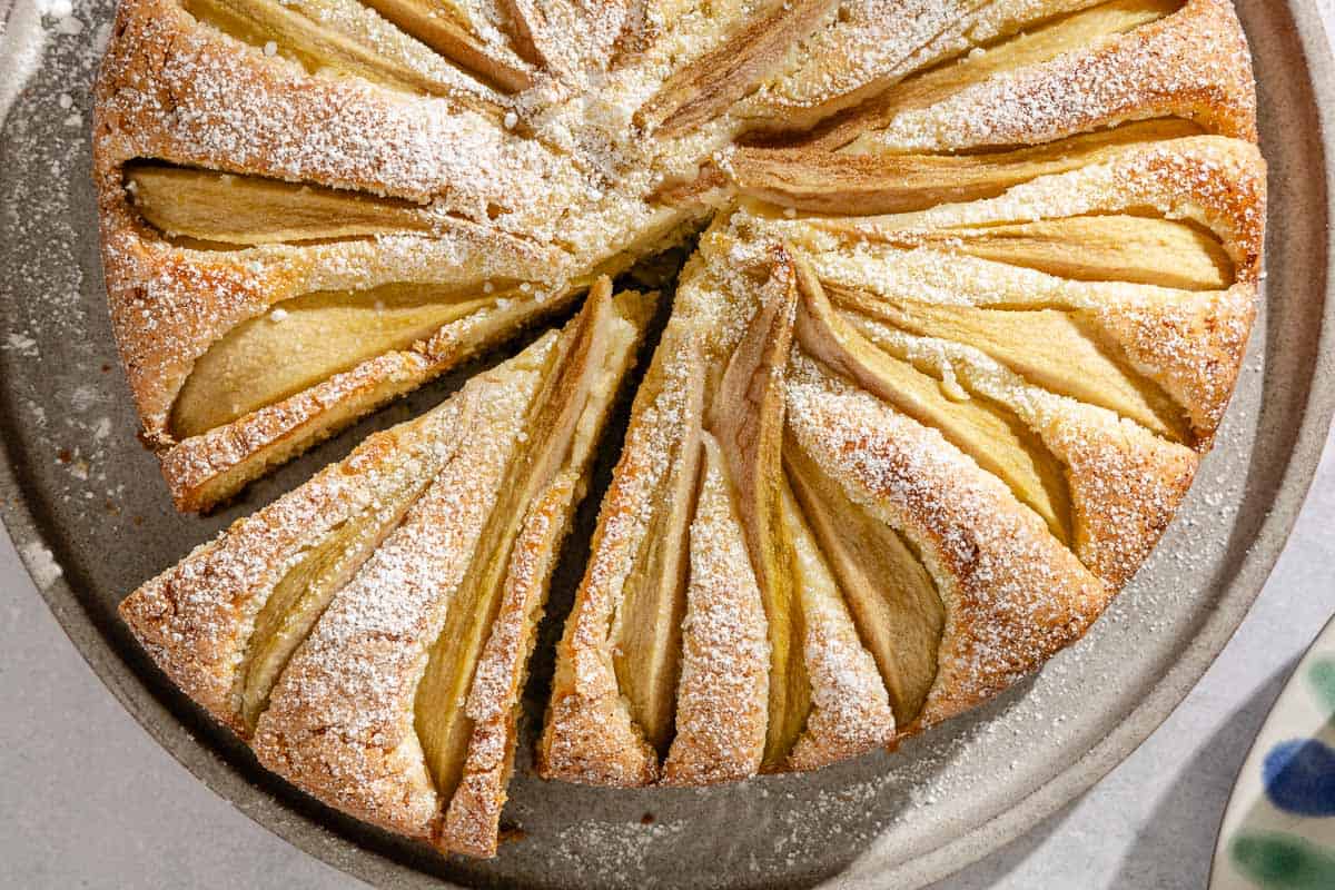 An Italian pear cake with one slice cut out of it on a serving platter.