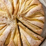 An Italian pear cake with one slice cut out of it on a serving platter.