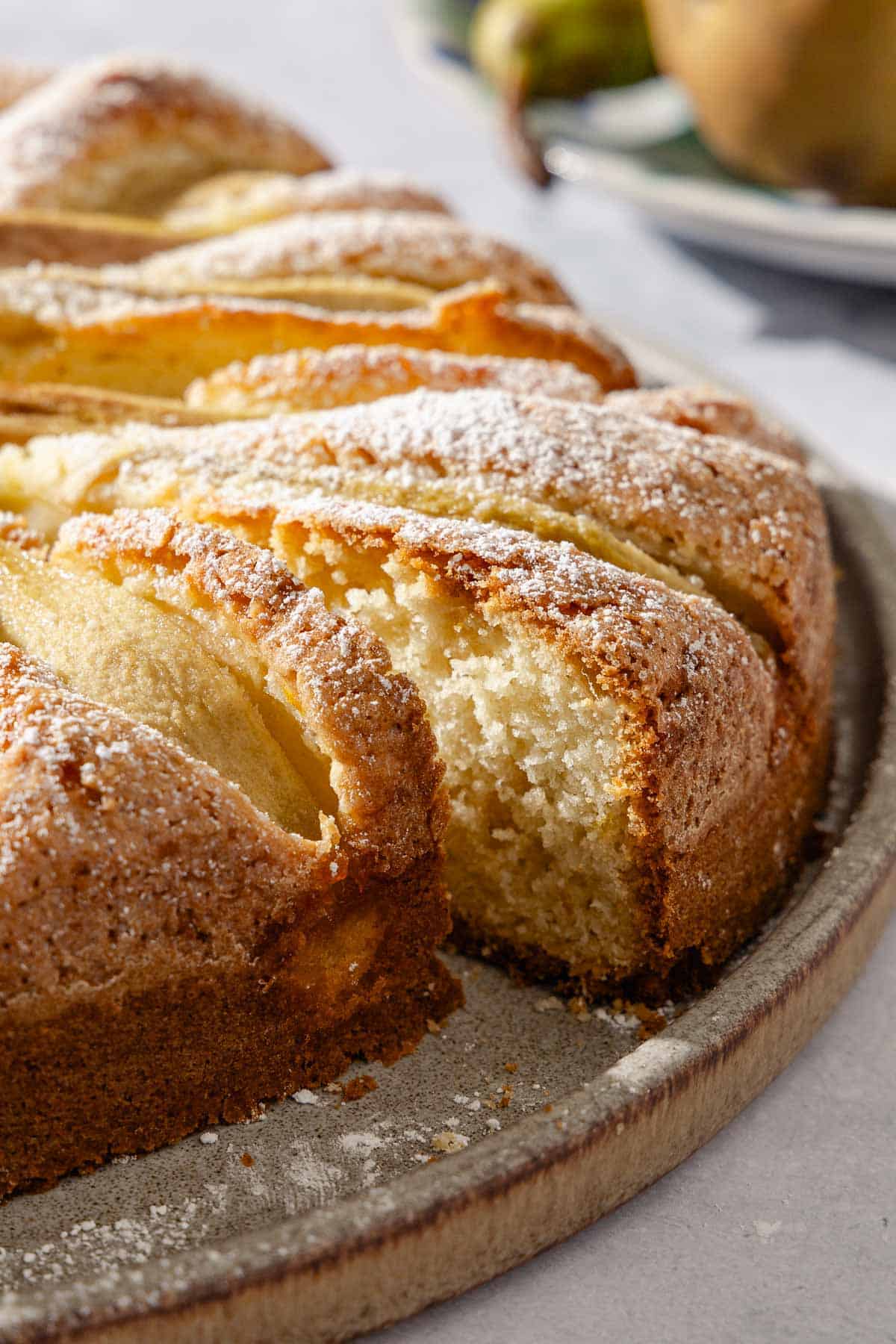 A close up of an Italian pear cake with one slice cut out of it on a serving platter.