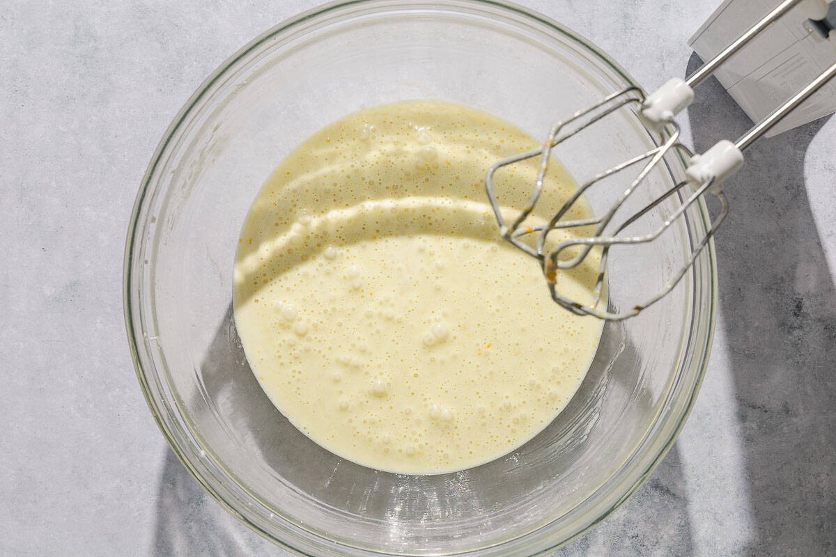 The wet ingredients for the Italian pear cake in a mixing bowl next to a hand mixer.