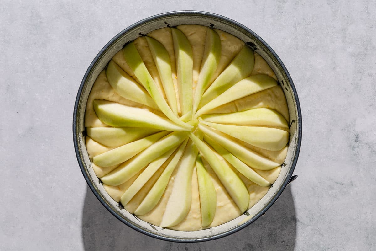 An overhead photo of the batter for the Italian pear cake topped with pear slices in a round baking pan.