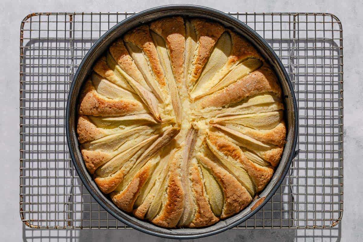 An Italian pear cake in a baking pan cooling on a wire rack.