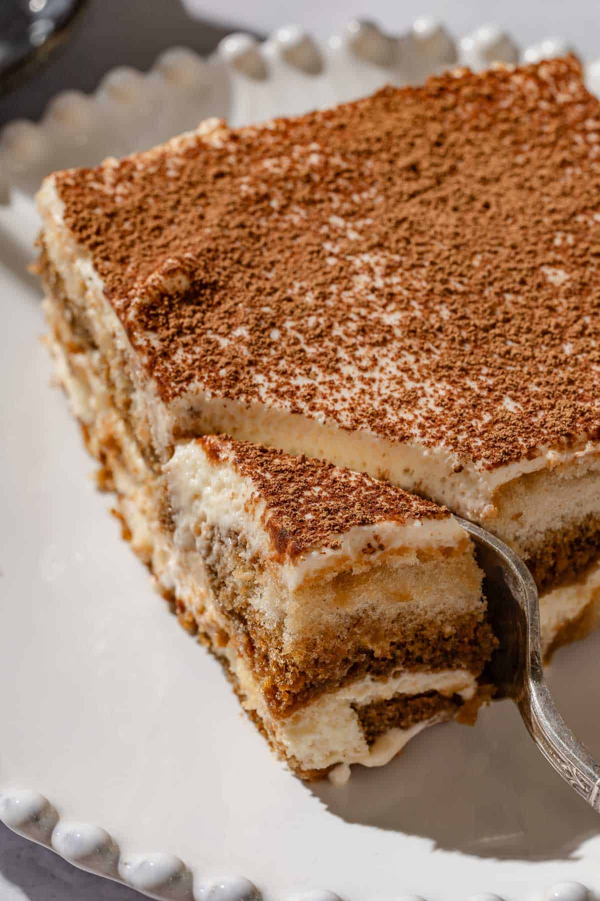 A close up of a slice of tiramisu on a plate with a fork.