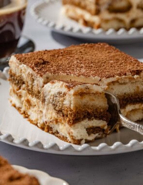 A close up of a slice of tiramisu on a plate with a fork.