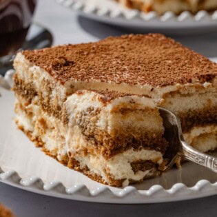 A close up of a slice of tiramisu on a plate with a fork.