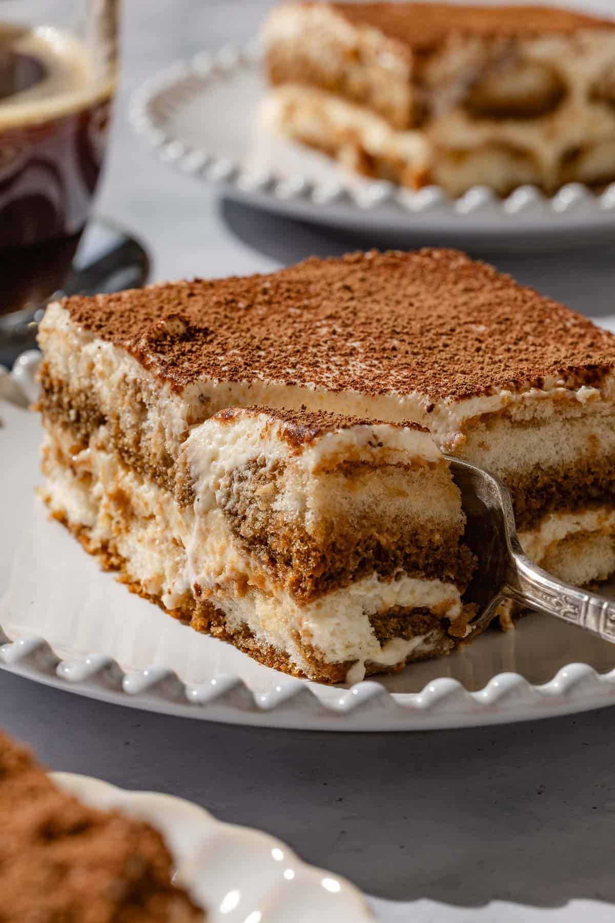 A close up of a slice of tiramisu on a plate with a fork.