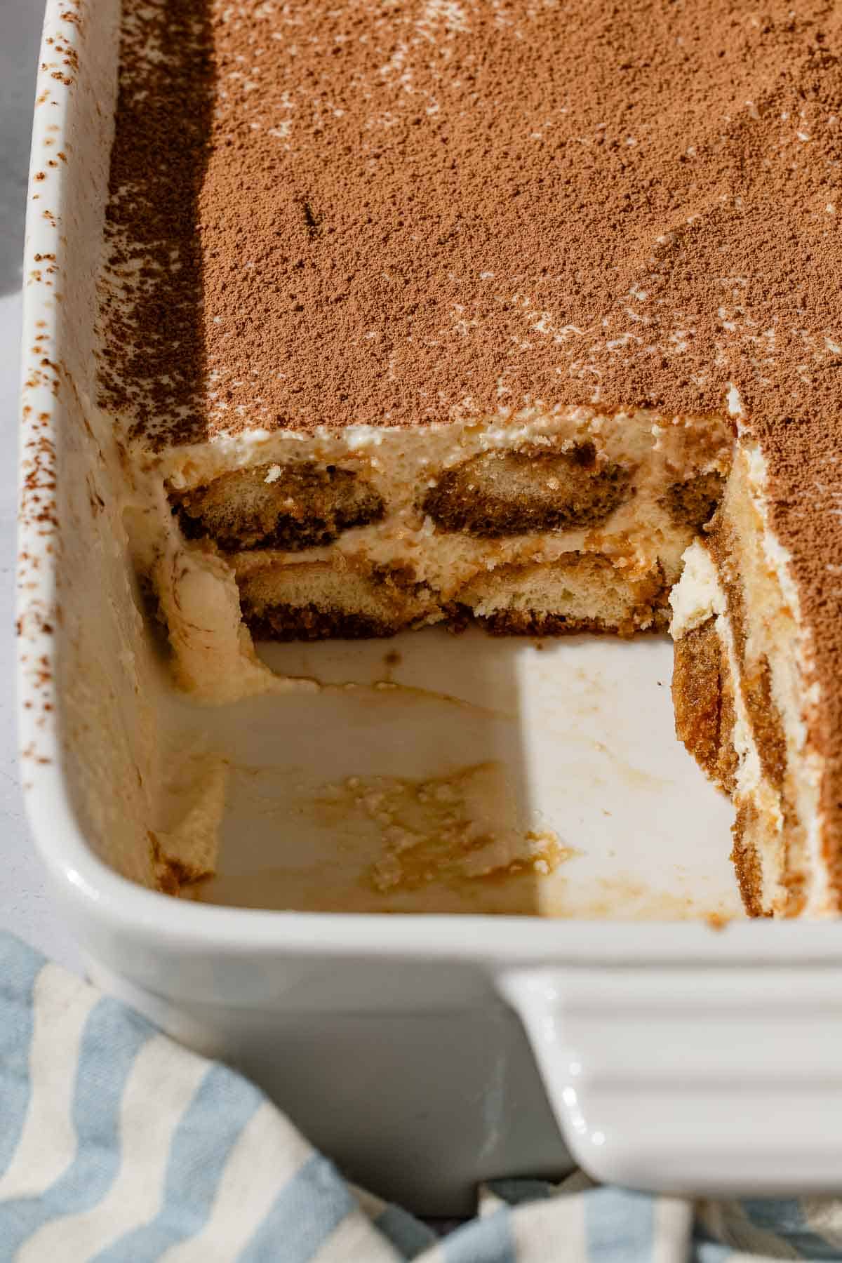 A close up of the tiramisu in a baking dish with one slice cut from it.