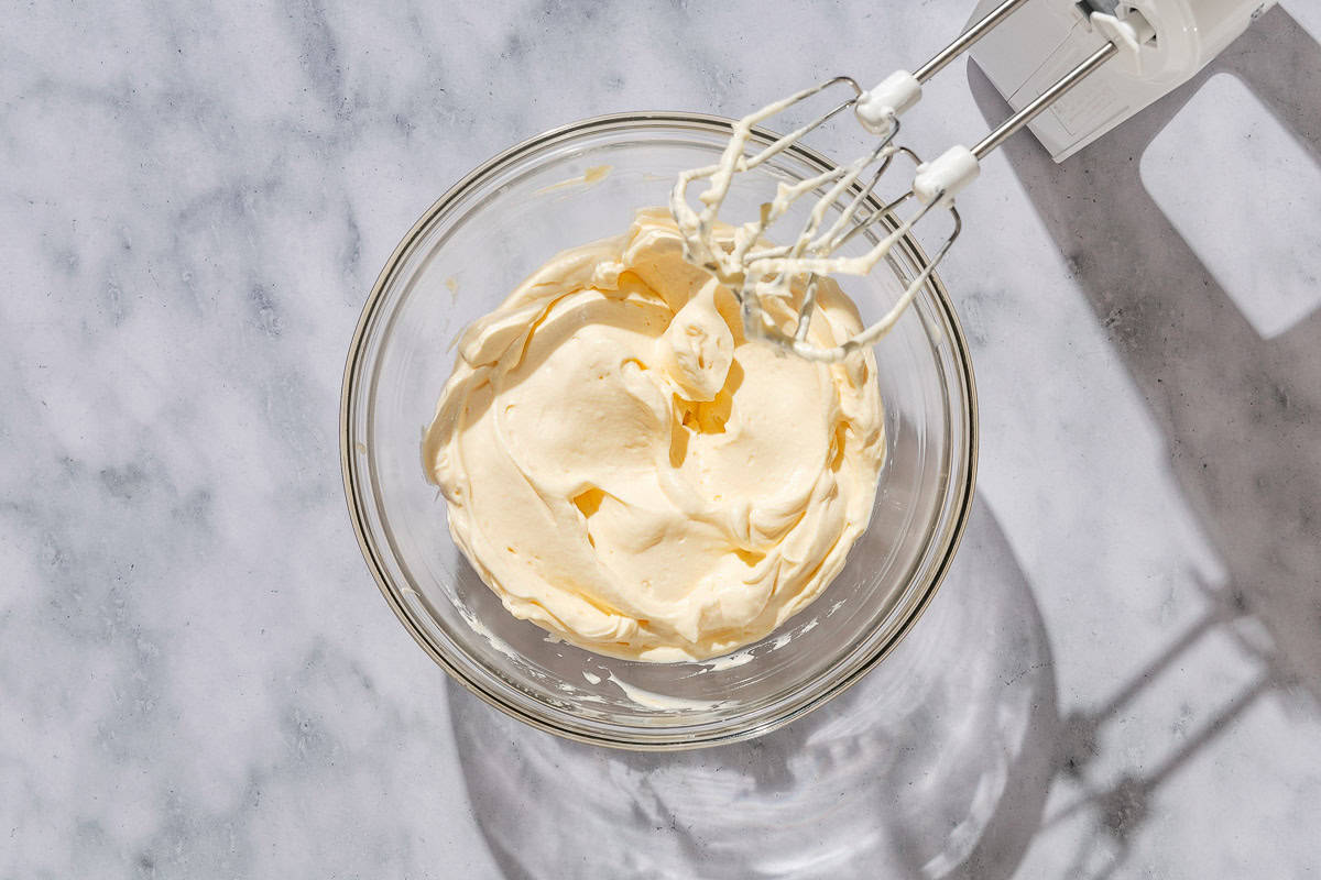 The yolk mixture combined with the mascarpone in a bowl. Next to this is a hand mixer.