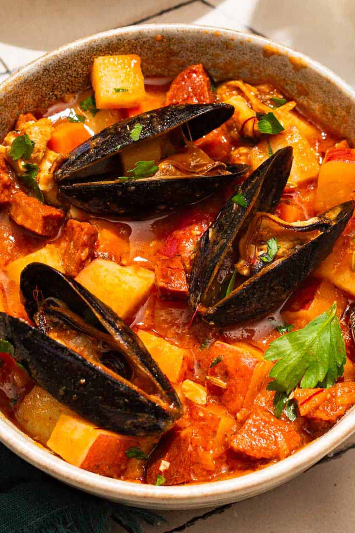 A close up of mussels with chorizo in a saffron stew in a bowl.