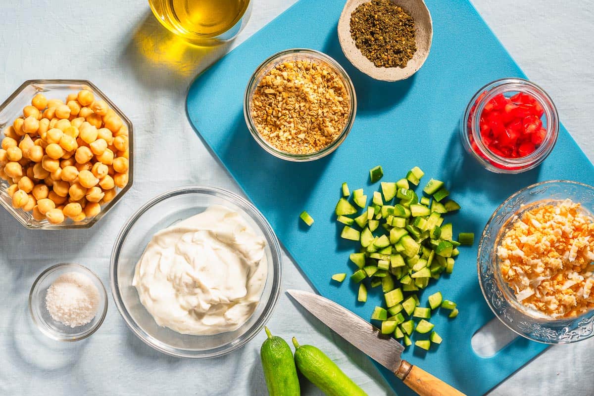 Ingredients for savory yogurt bowls including greek yogurt, chickpeas, hard boiled eggs, persian cucumbers, roma tomatoes, olive oil, kosher salt, za'atar, and dukkah.