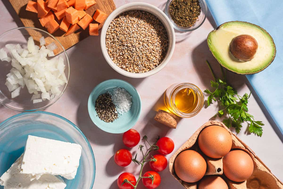 Ingredients for savory oatmeal including steel cut oats, olive oil, onion, sweet potato, salt, black pepper, eggs, avocado, cherry tomatoes, parsley, feta cheese and za'atar.