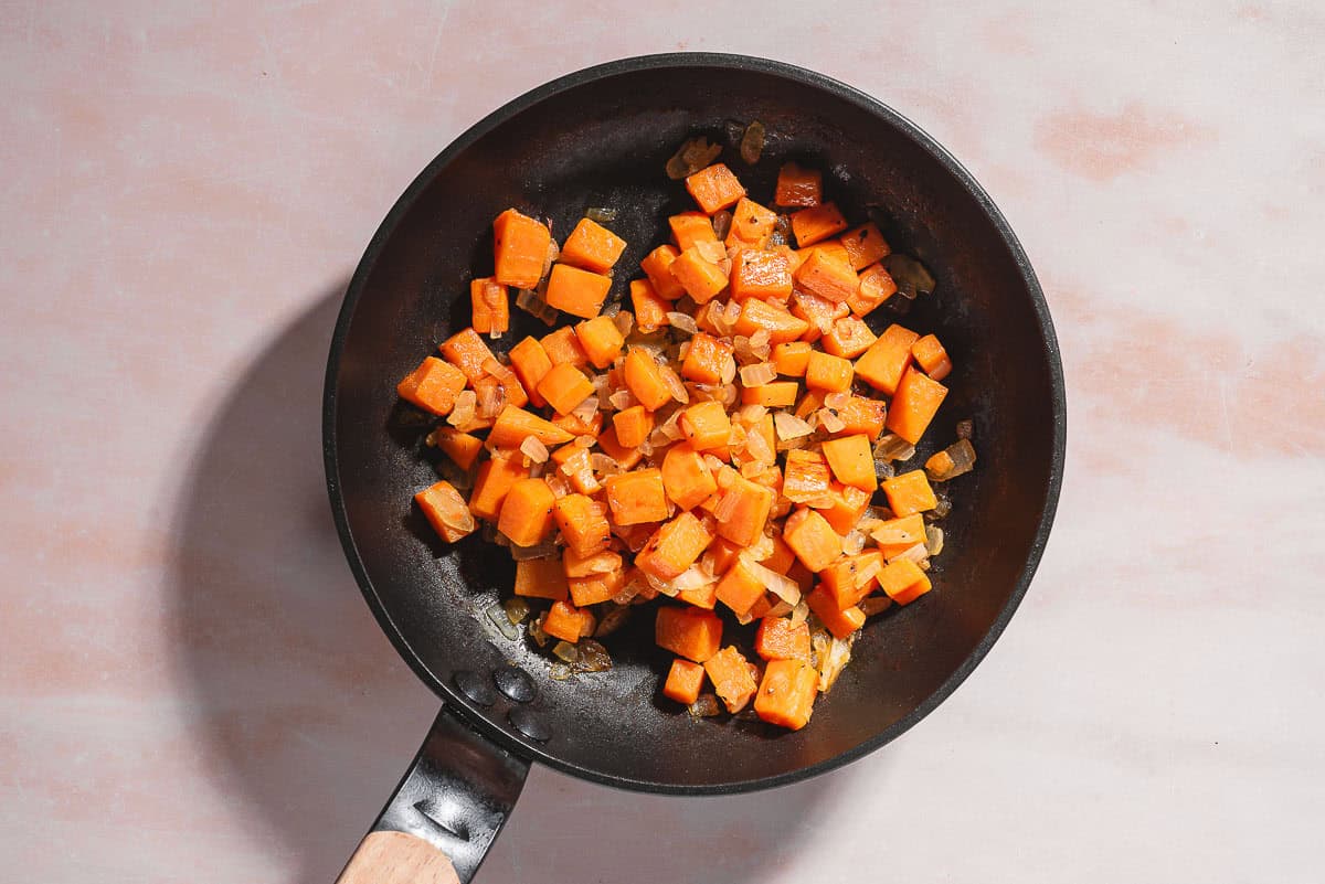 An overhead photo of chopped sweet potatoes and onions in a skillet.