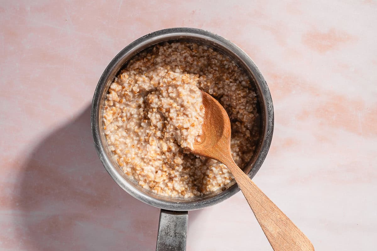 An overhead photo of cooked steel cut oats in a saucepan with a wooden spoon.