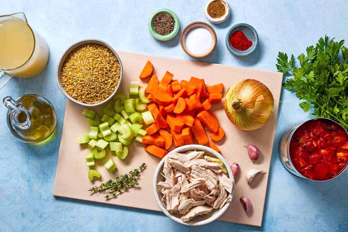 Ingredients for freekeh soup with chicken including freekeh, chicken, onion, celery, carrots, garlic, olive oil, salt, fire roasted tomatoes, chicken broth, black pepper, sweet paprika, cumin, thyme, and parsley.