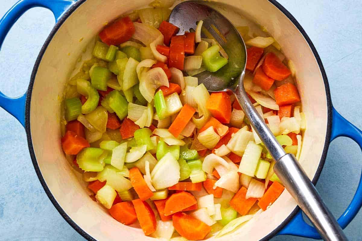 An overhead photo of the vegetables for the freekeh soup with chicken being softened in a large pot with a slotted spoon.