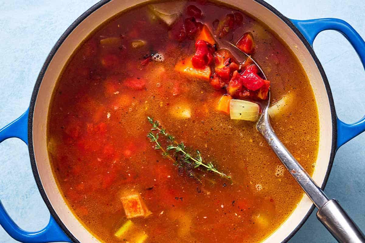 An overhead photo of freekeh soup with chicken cooking in a large pot with a slotted spoon.