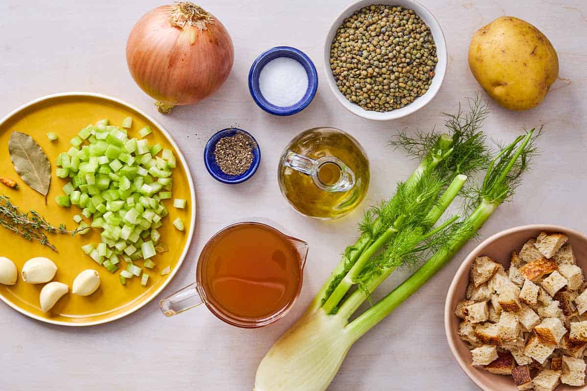 Ingredients for lentil potato soup including lentils, potato, olive oil, garlic, celery, onion, fennel, peperoncino, thyme, a bay leaf, salt, broth, cubed bread, and black pepper.