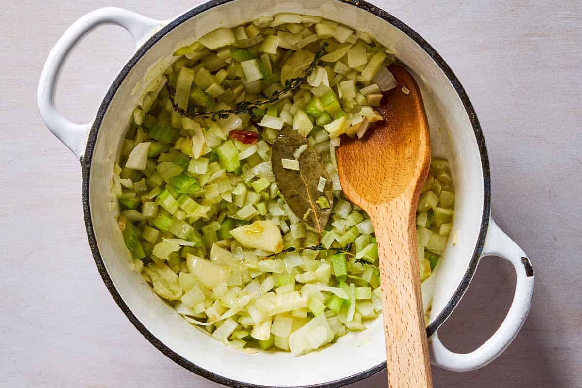 The aromatics for the soup being sauteed in a pot with a wooden spoon.