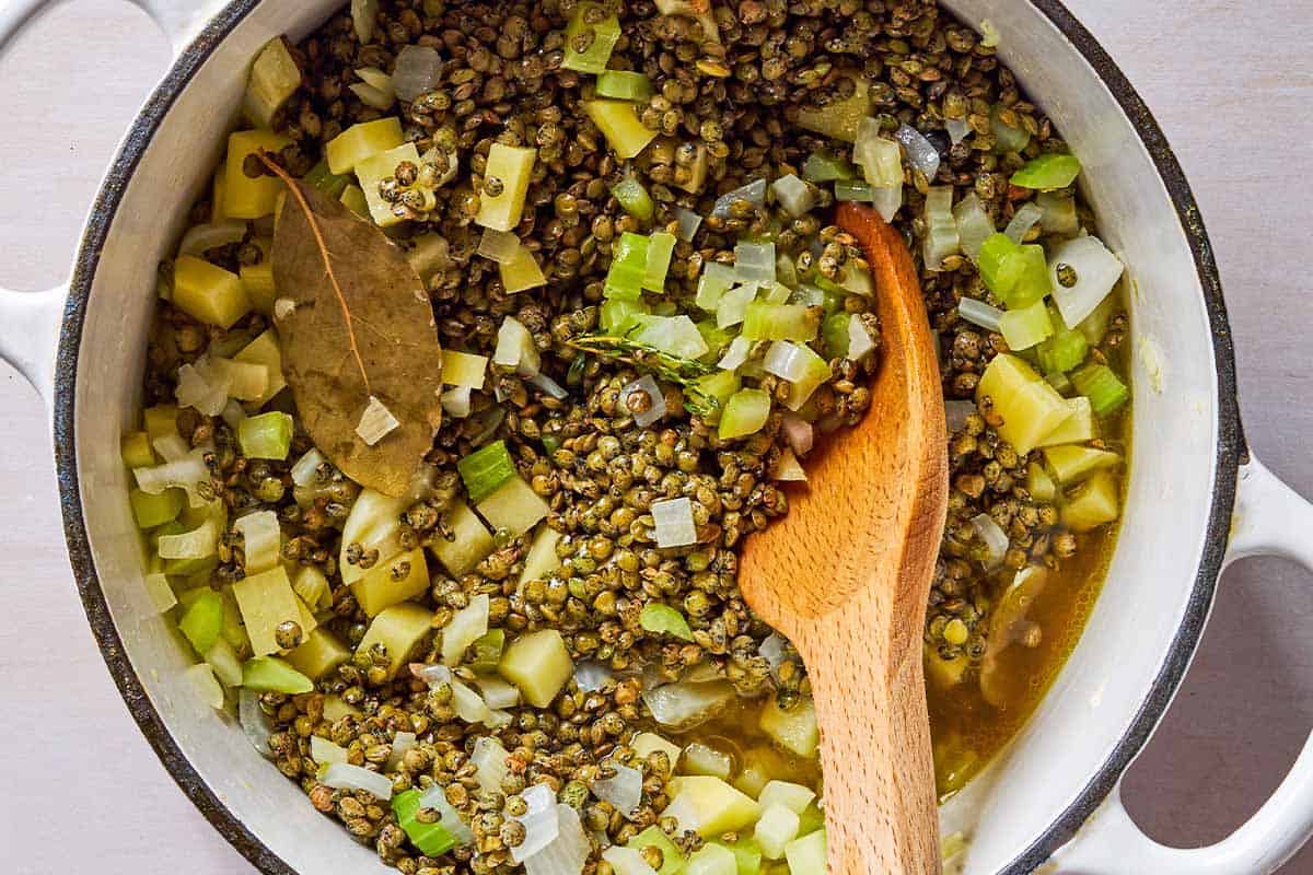 The aromatics, potatoes and lentils for the soup being sauteed in a pot with a wooden spoon.