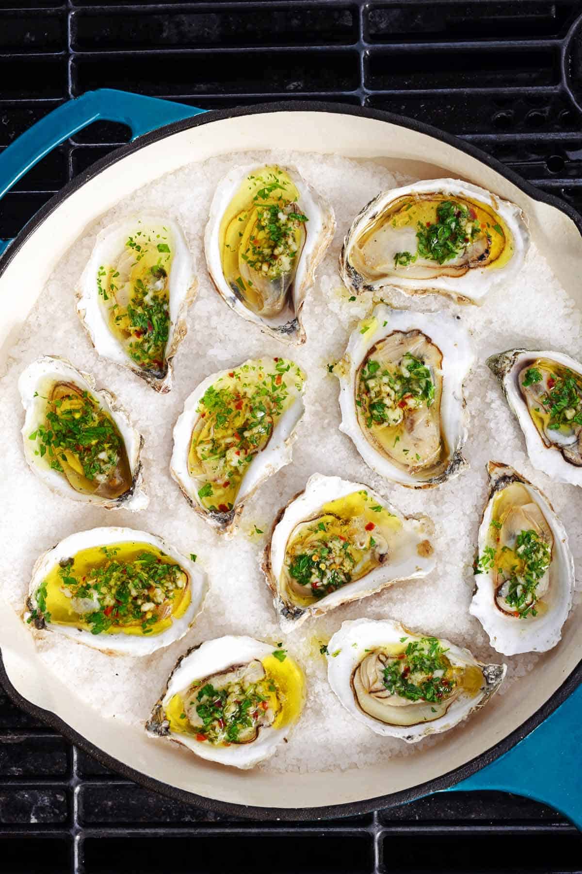 Overhead shot of 12 oysters in a blue pan on a grill.