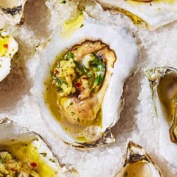 A close up of several grilled oysters with garlicky herb sauce on a bed of rock salt.