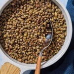 An overhead photo of green lentils in a saucepan with a spoon next to a cloth napkin.