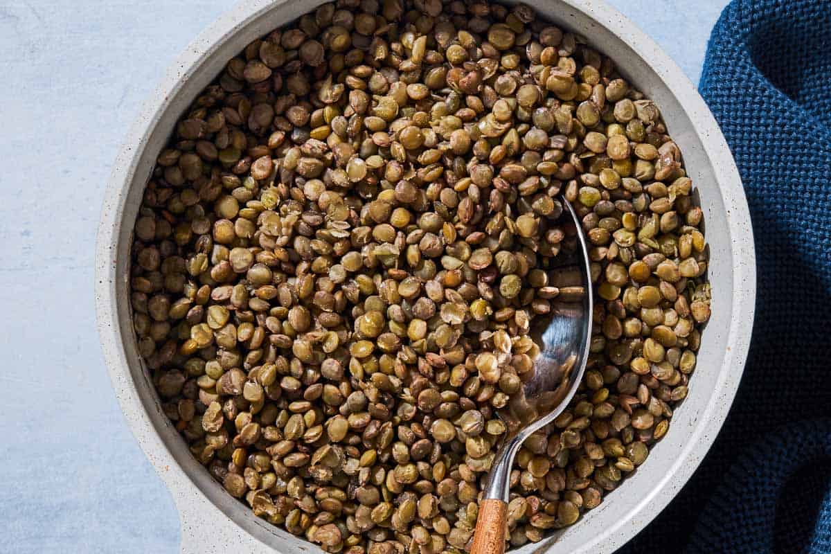 An overhead photo of green lentils in a bowl with a spoon next to a cloth napkin.