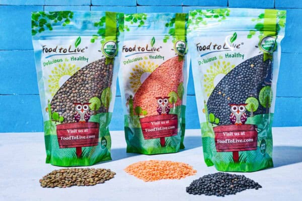 A close up of packages of green lentils, red lentils and black lentils, each with a handful of the corresponding lentil type in front of it.