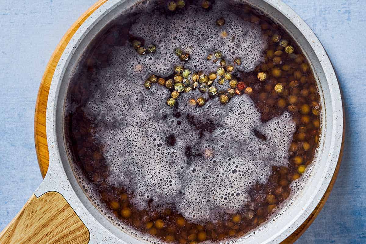 An overhead photo of green lentils cooking in water in a saucepan.